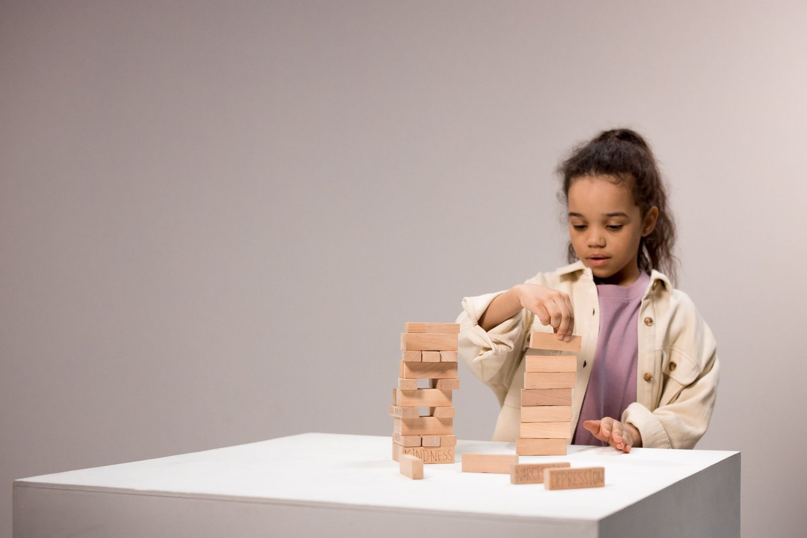 A child carefully stacks wooden blocks indoors, concentrating on her play and creativity.