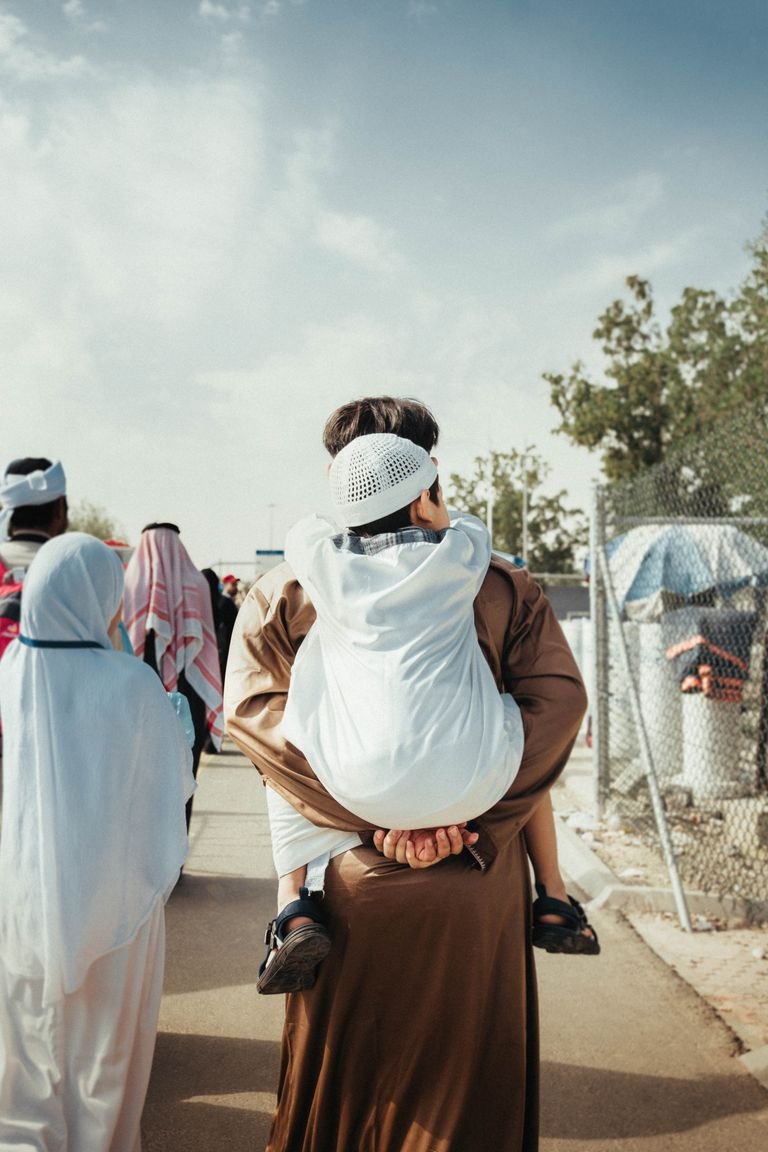 A father carrying his child outdoors, showcasing traditional Middle Eastern attire.