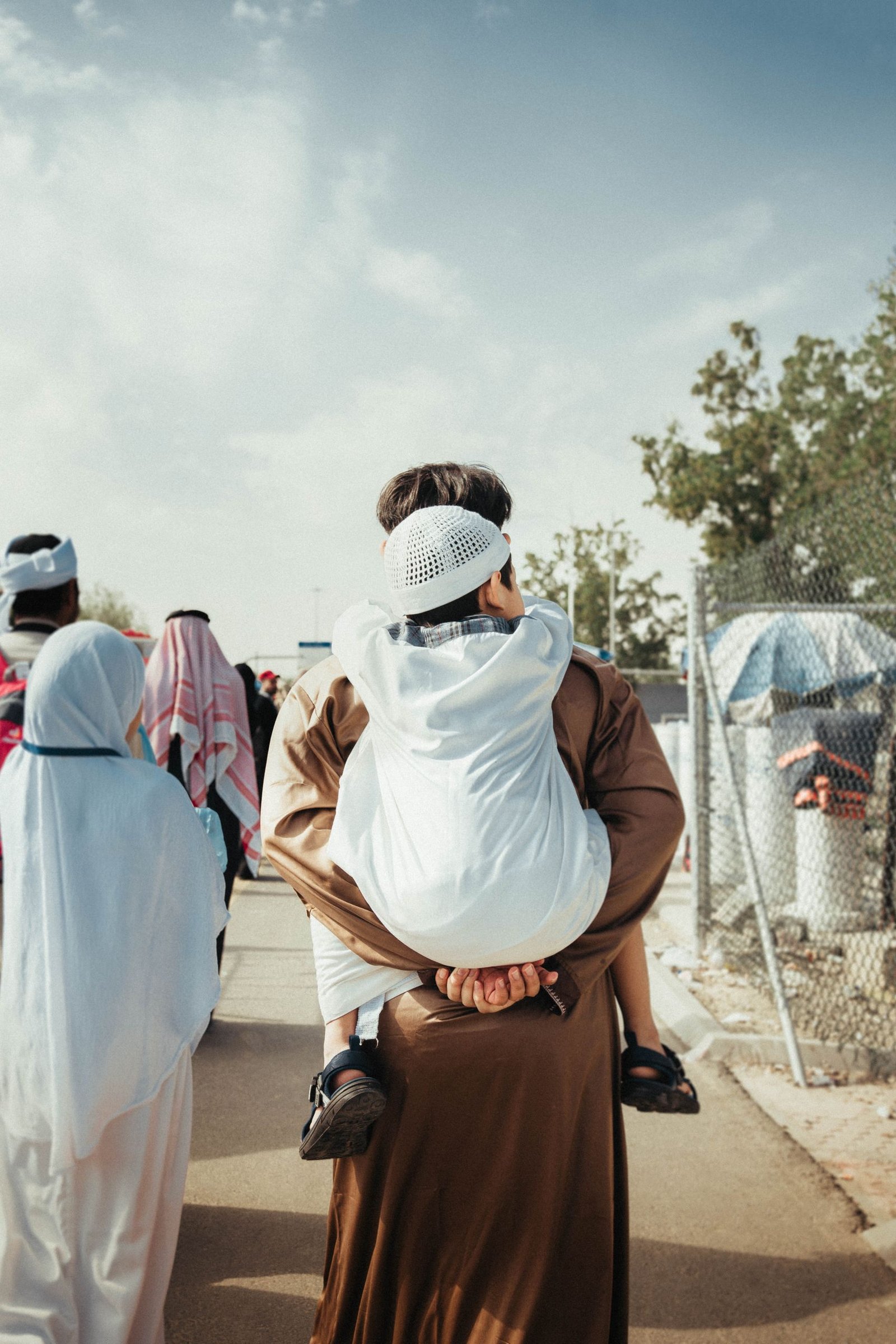 A father carrying his child outdoors, showcasing traditional Middle Eastern attire.