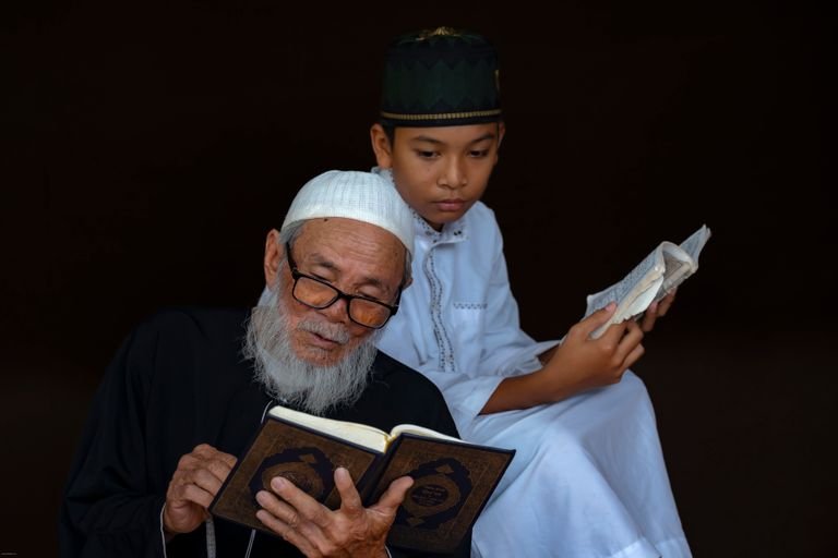 An elderly man and young boy in traditional attire reading religious texts together, conveying wisdom and tradition.