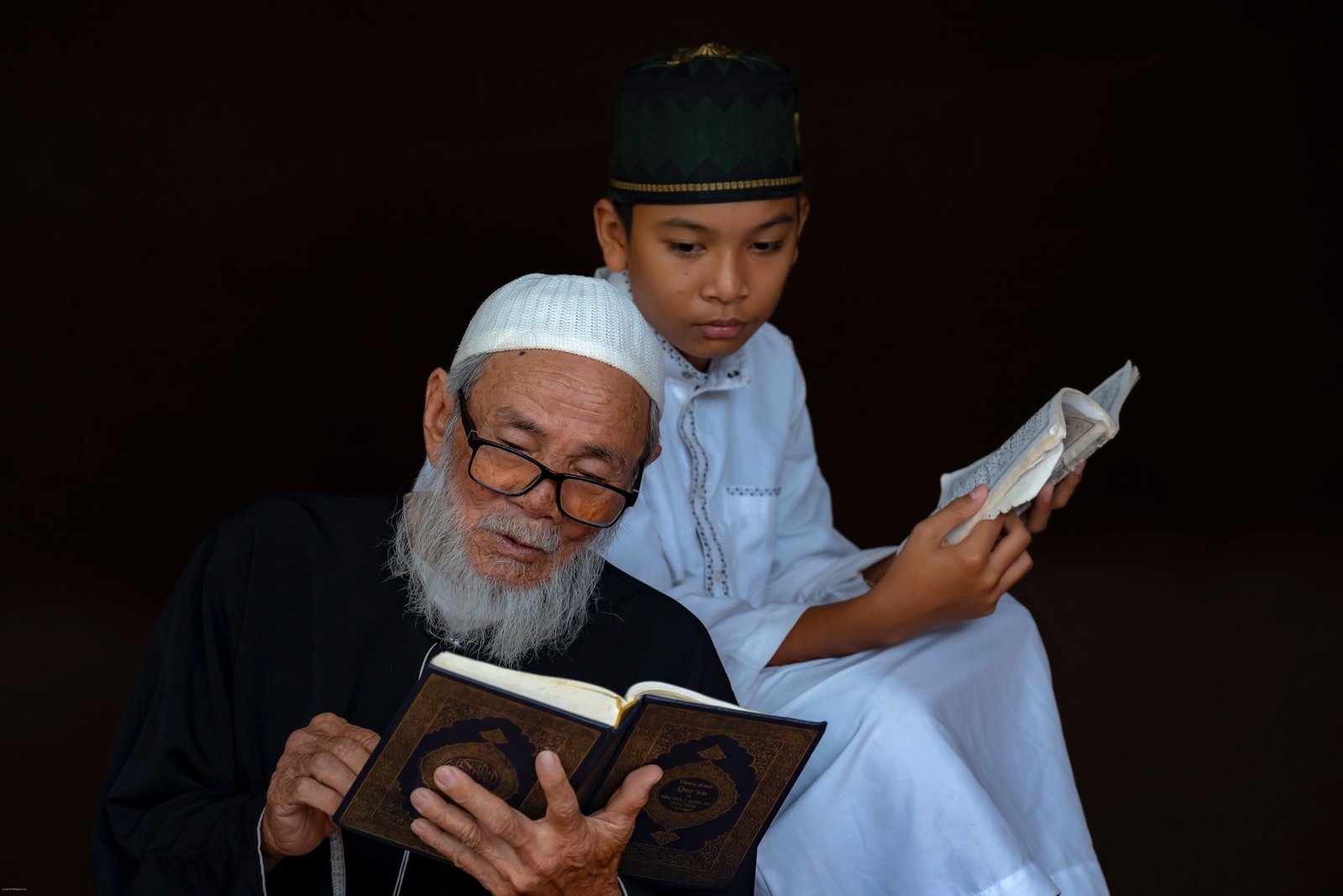 An elderly man and young boy in traditional attire reading religious texts together, conveying wisdom and tradition.